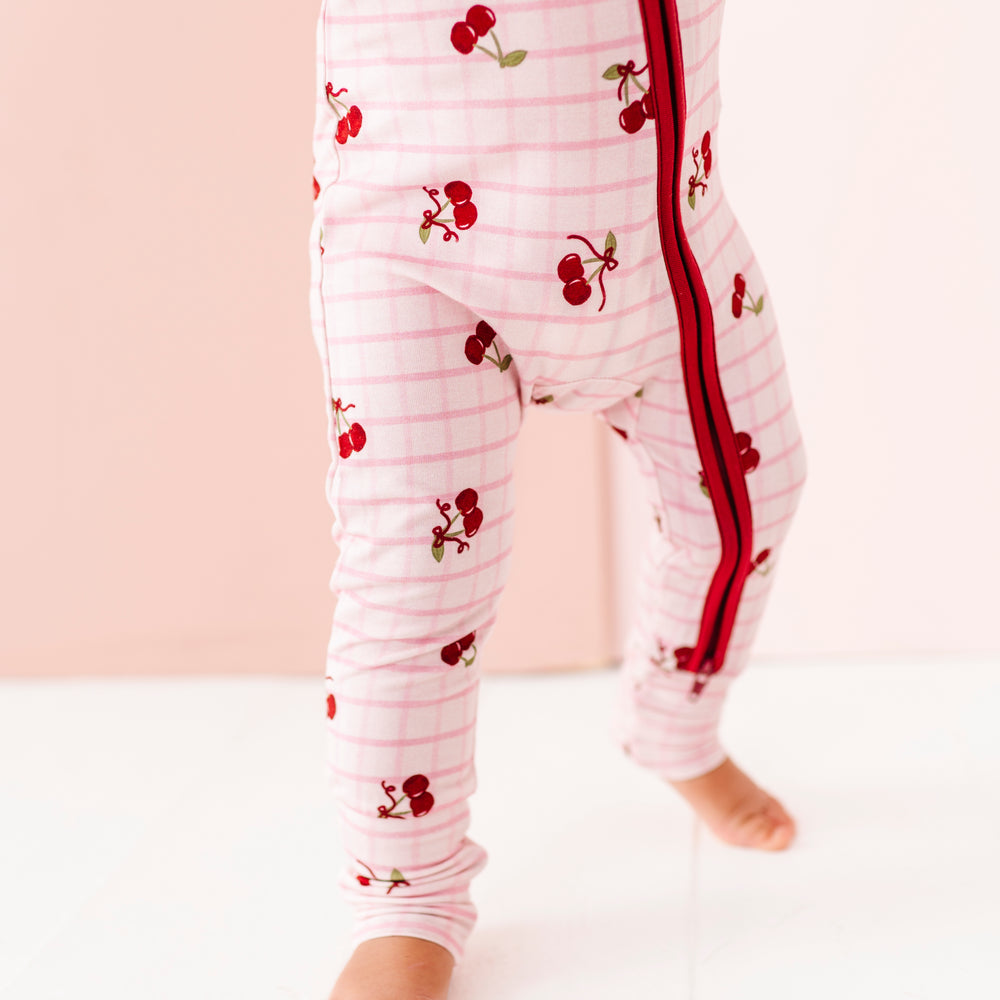 
                      
                        Baby wearing a white onesie with red cherry pattern on a light pink background
                      
                    
