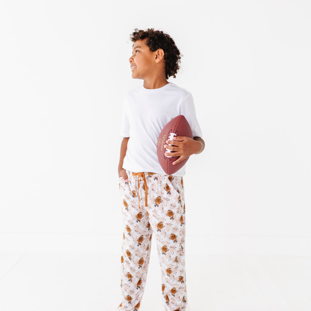 
                      
                        Person wearing a white t-shirt and patterned pajama pants holding a football on a white background
                      
                    