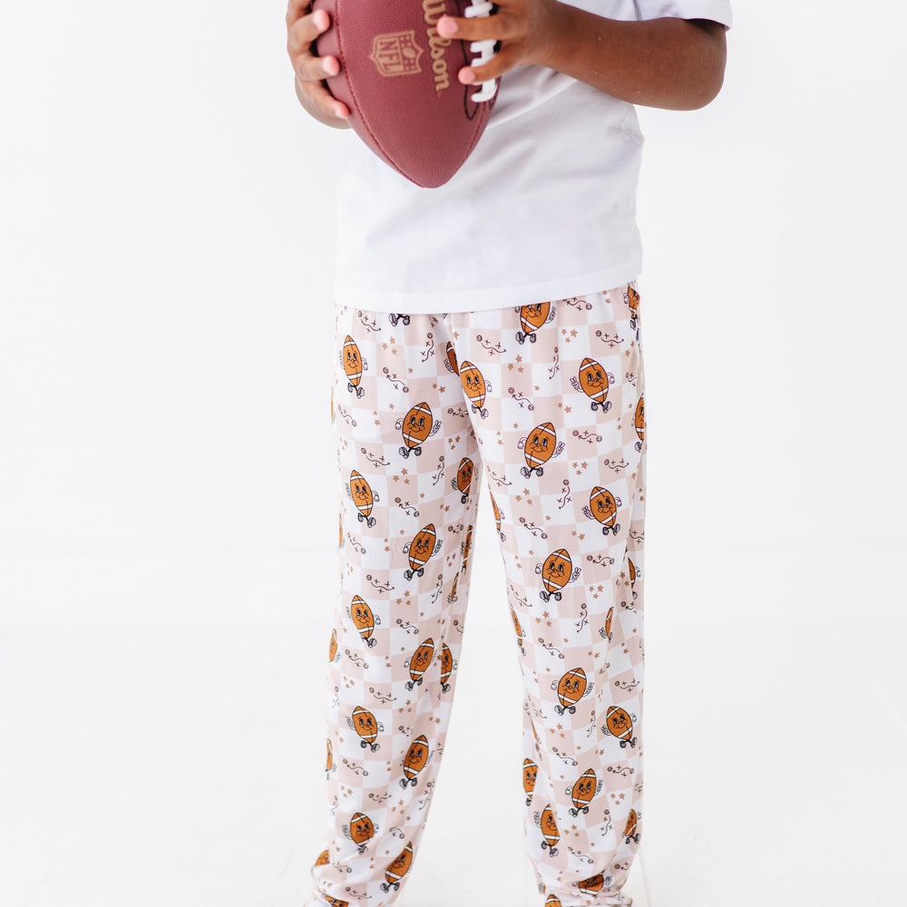 Person wearing pajama pants with a football pattern, holding a red football on a white background