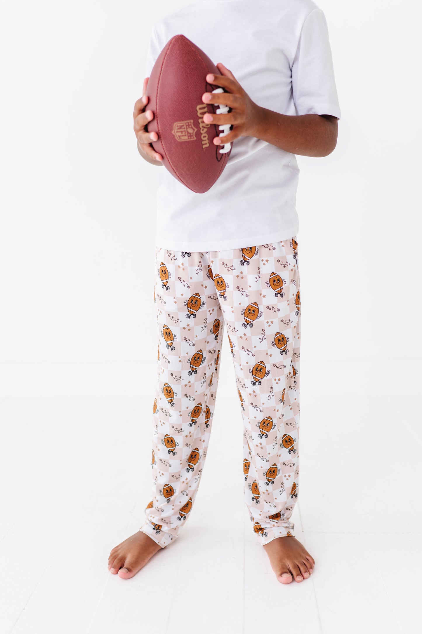 Person wearing pajama pants with a football pattern, holding a red football on a white background