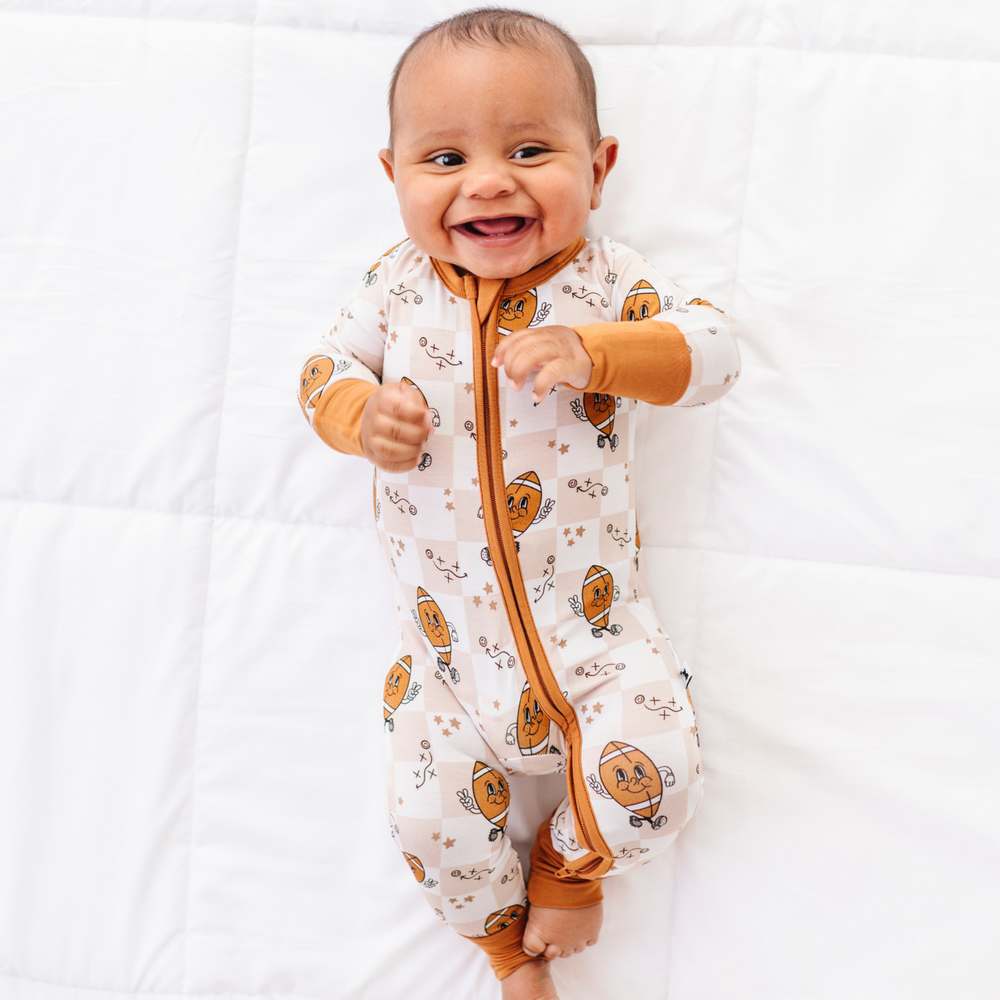 Baby wearing a white onesie with orange patterns and a zipper, smiling on a white background
