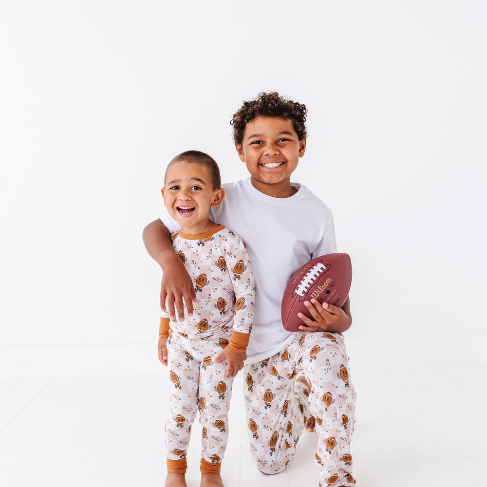 
                      
                        Two children in matching pajamas with one holding a football on a white background
                      
                    