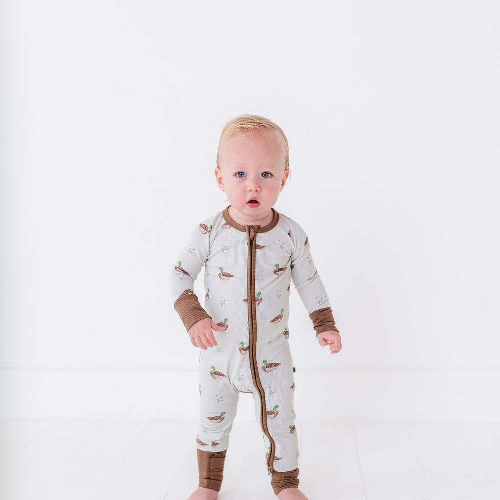 
                      
                        Baby wearing a white onesie with brown accents on a white background
                      
                    
