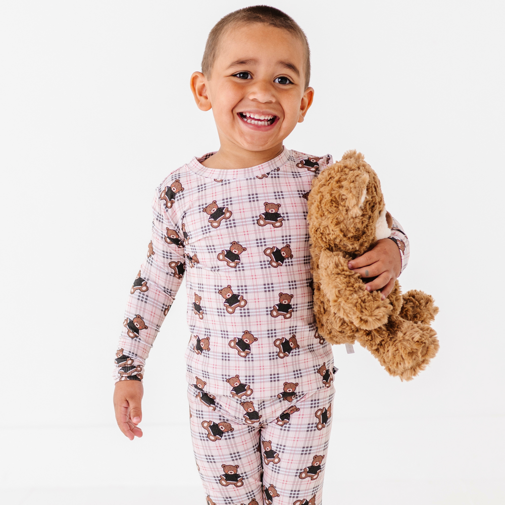 Child wearing pajamas with teddy bear pattern holding a teddy bear on a white background