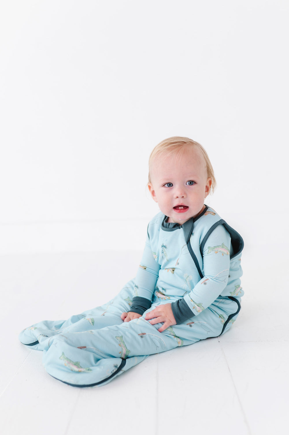 Baby in a blue sleeping bag with fish pattern on a white background