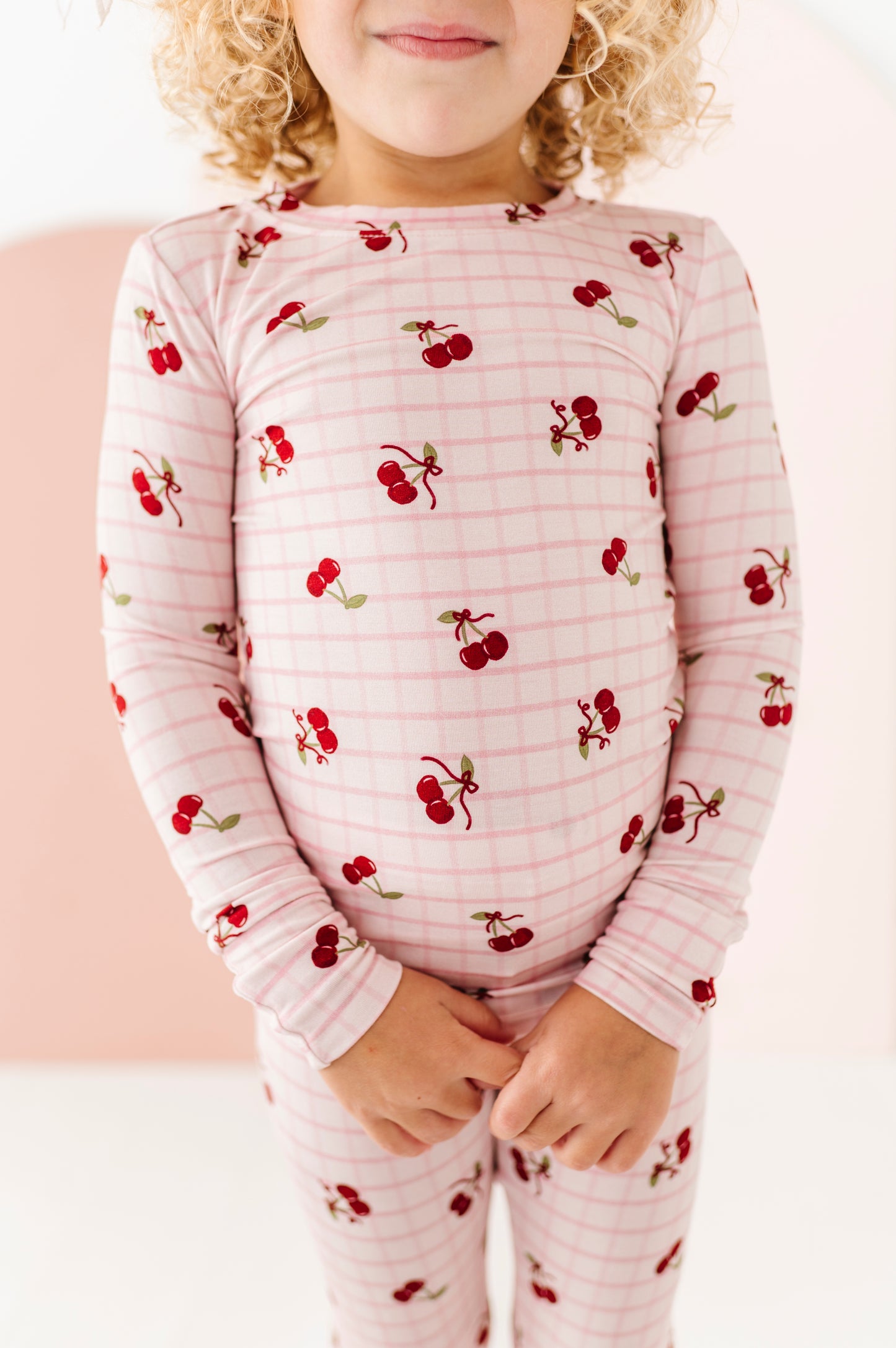Child wearing a pink pajama set with cherry pattern against a white background