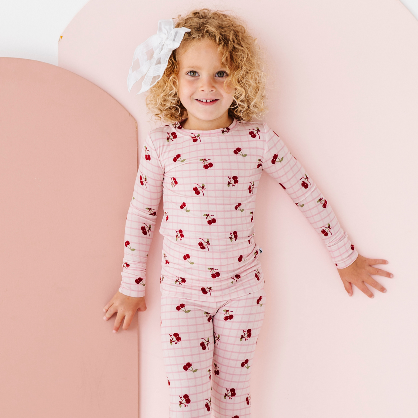 Child wearing a pink and red striped pajama set with cherry pattern on a pink background