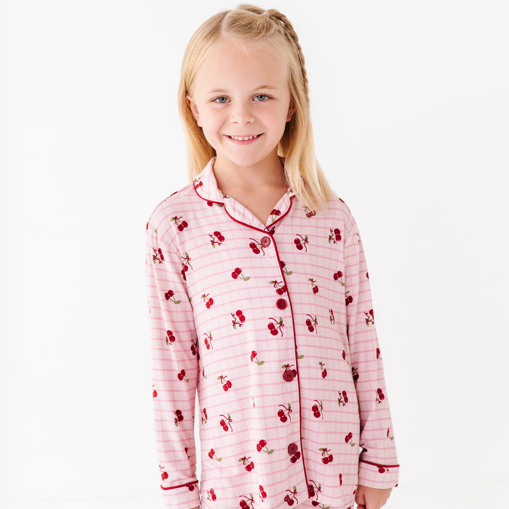 
                      
                        Young girl wearing pink pajamas with cherry pattern on a white background
                      
                    