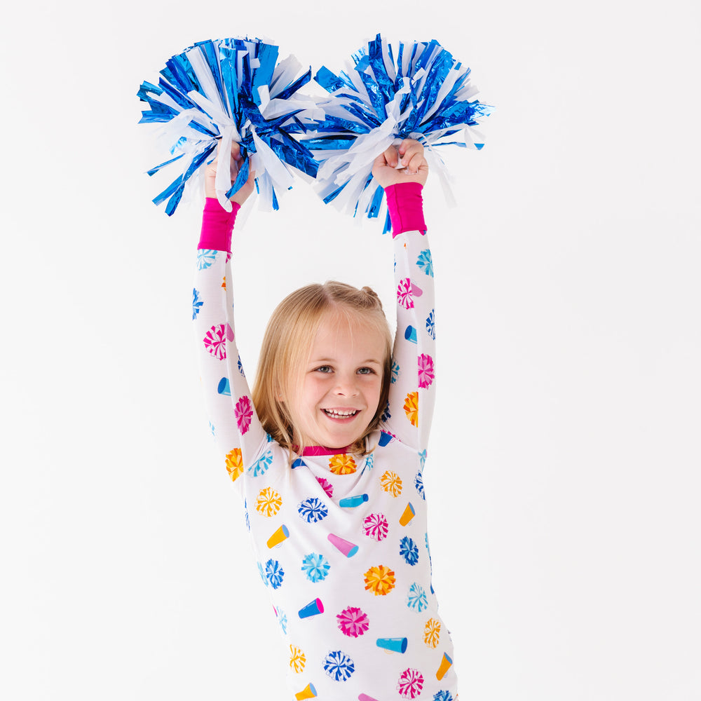 
                      
                        Child wearing colorful pajamas holding blue pom-poms against a white background
                      
                    