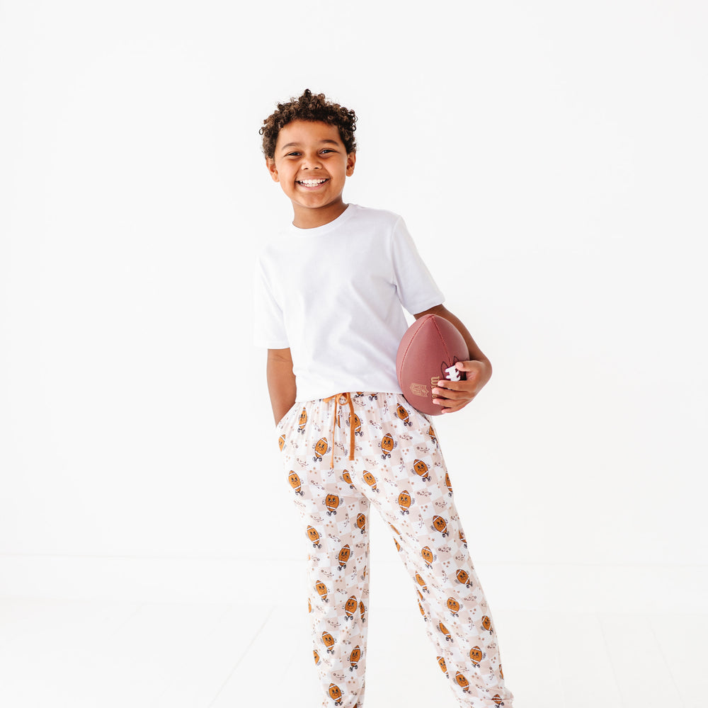 
                      
                        Child wearing a white t-shirt and patterned pajama pants holding a football on a white background
                      
                    
