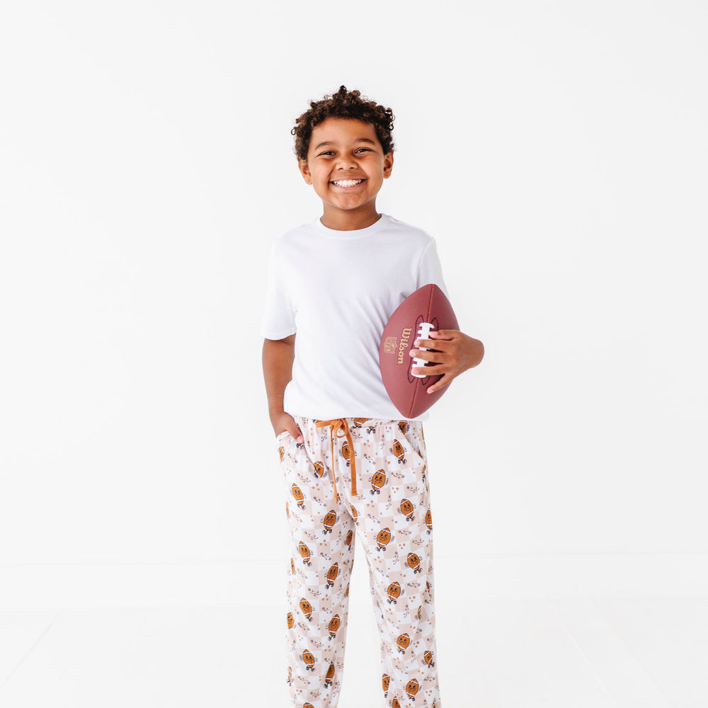 
                      
                        Child holding a football wearing a white t-shirt and patterned pajama pants on a white background
                      
                    